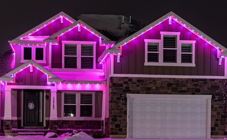 Two-story home washed in magenta roofline lighting